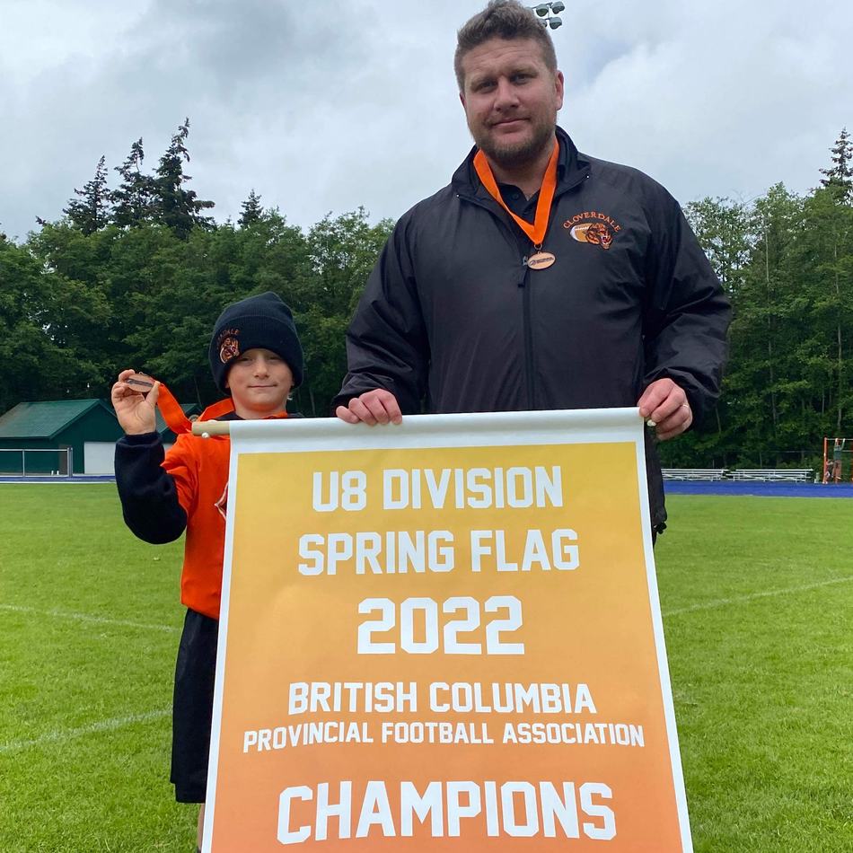 Coach Steven Sapinsky holding the 2022 U8 Spring Flag BC Provincial Champions banner with a young player