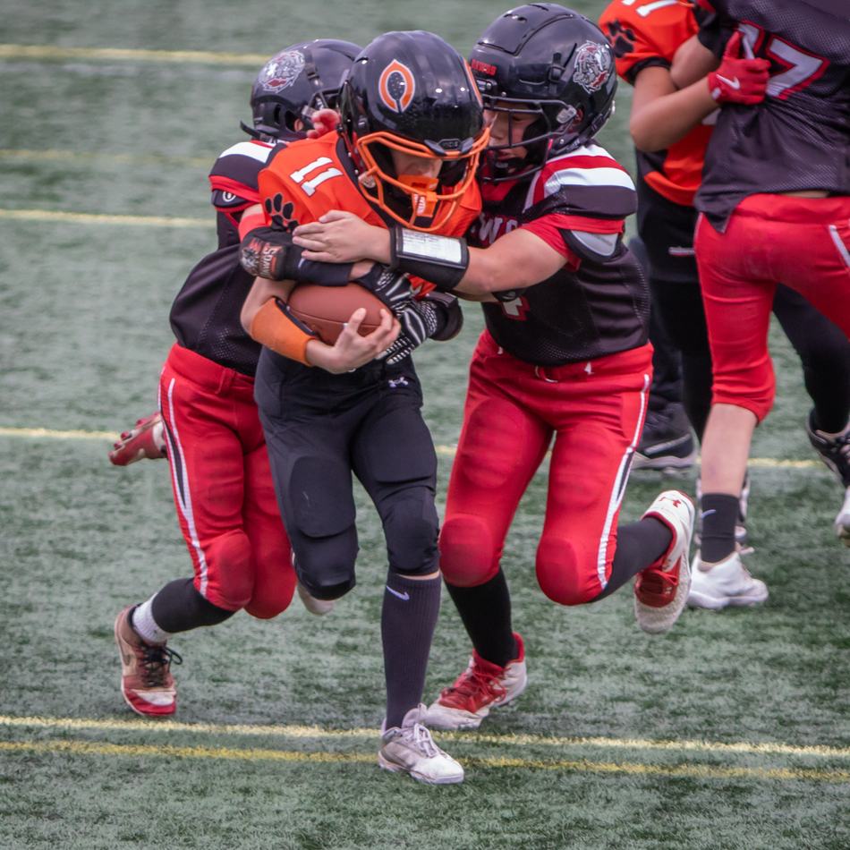 Youth tackle football players mid-play, ball carrier fighting through two tacklers